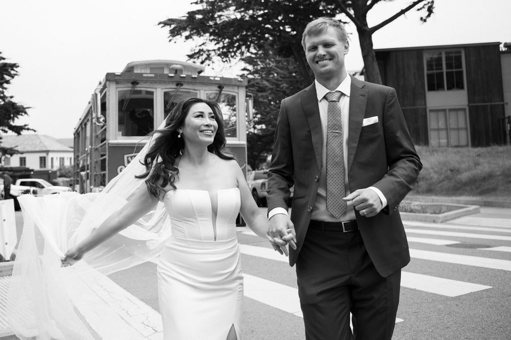 Candid black and white photo of bride and groom running with a San Francisco trolley behind them