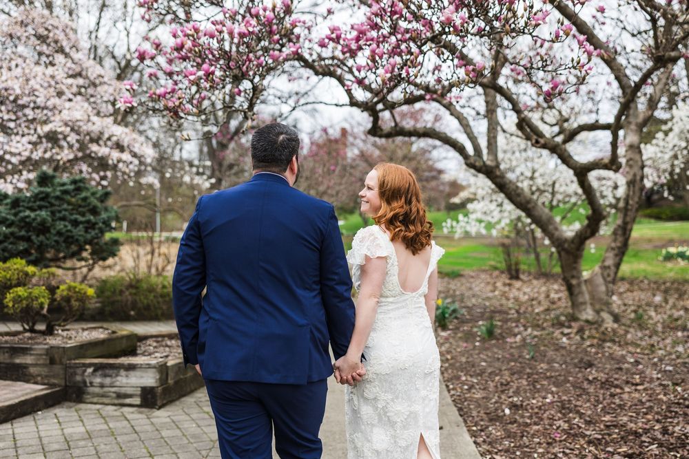 Couple walking hand in hand among blooming magnolia trees in a garden park setting.