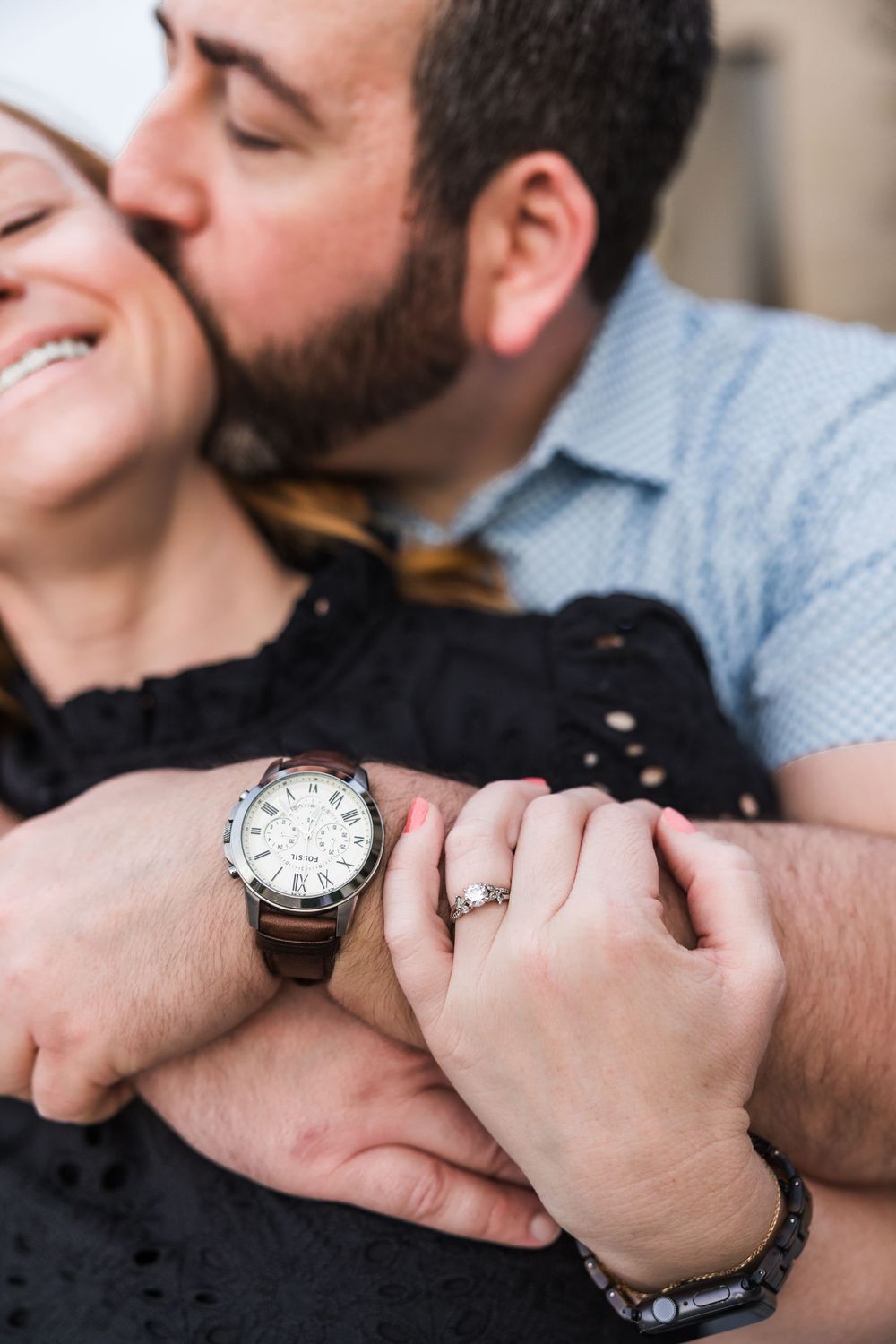 Close-up of engaged couple holding hands showing diamond ring and watch during romantic embrace.