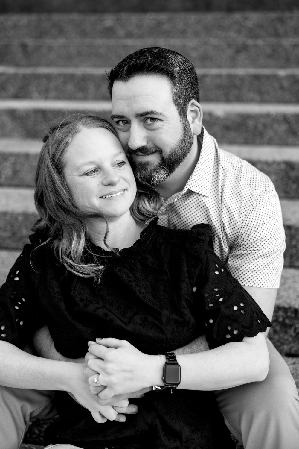Black and white portrait of smiling couple sitting together on stone steps in loving embrace.