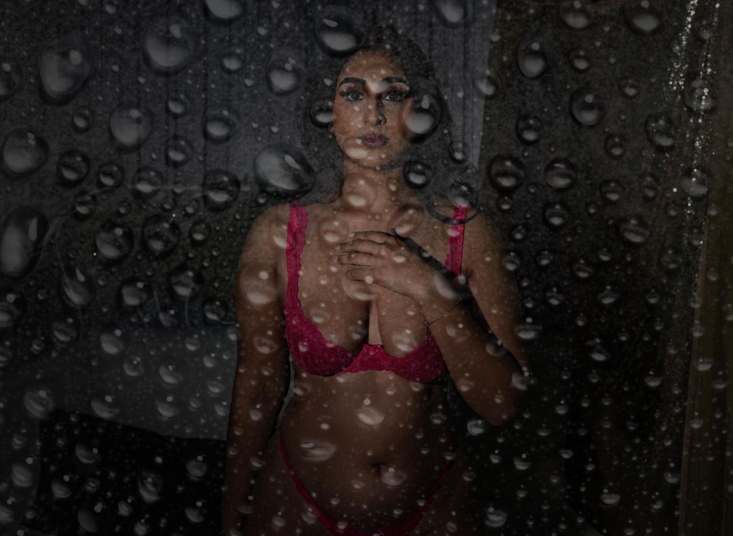 Empowering boudoir portrait of a woman with soft lighting and sultry pose with rain droplets