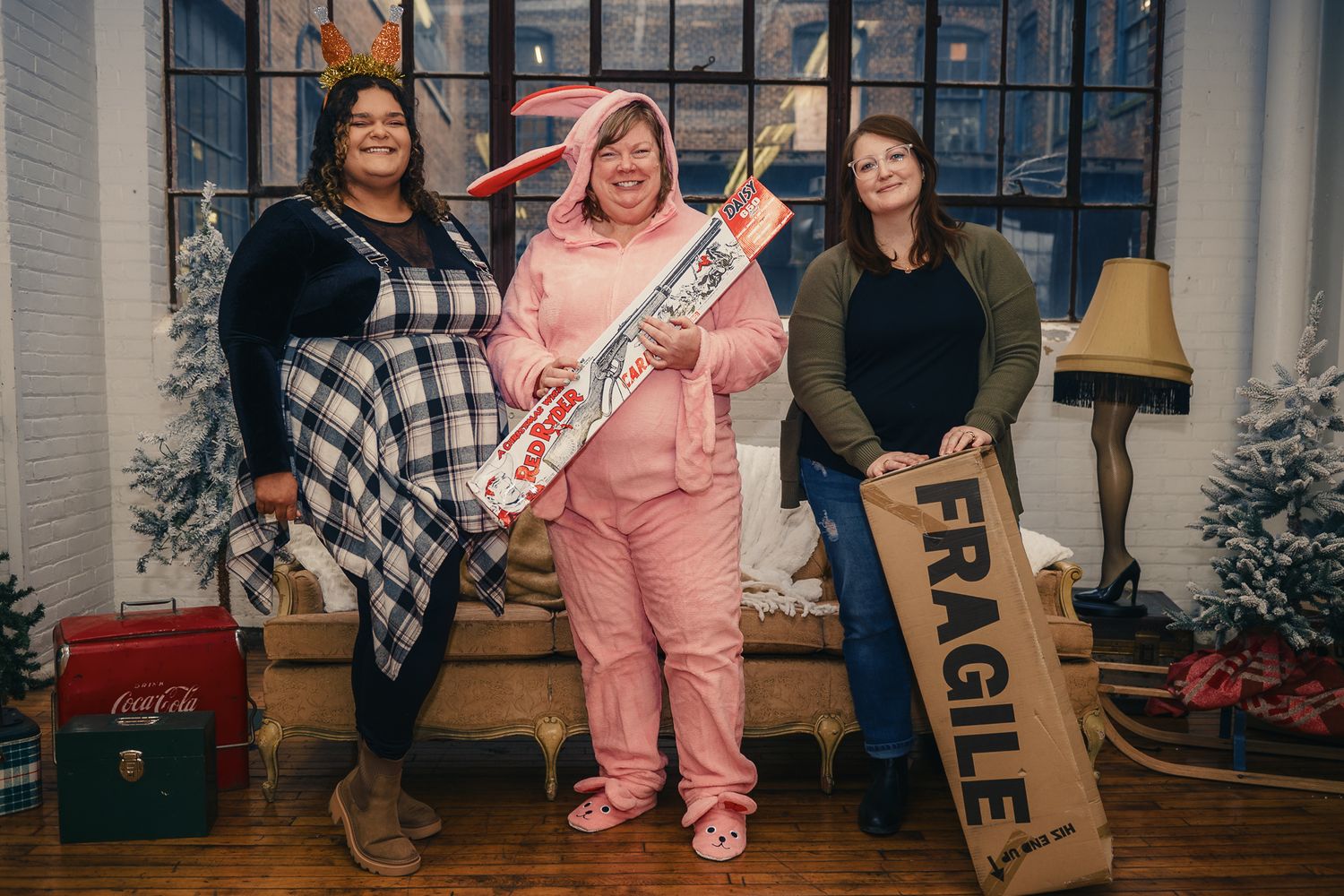 Three companions pose together on a porch with holiday decor, one holding a festive nutcracker and another with a wooden sign.