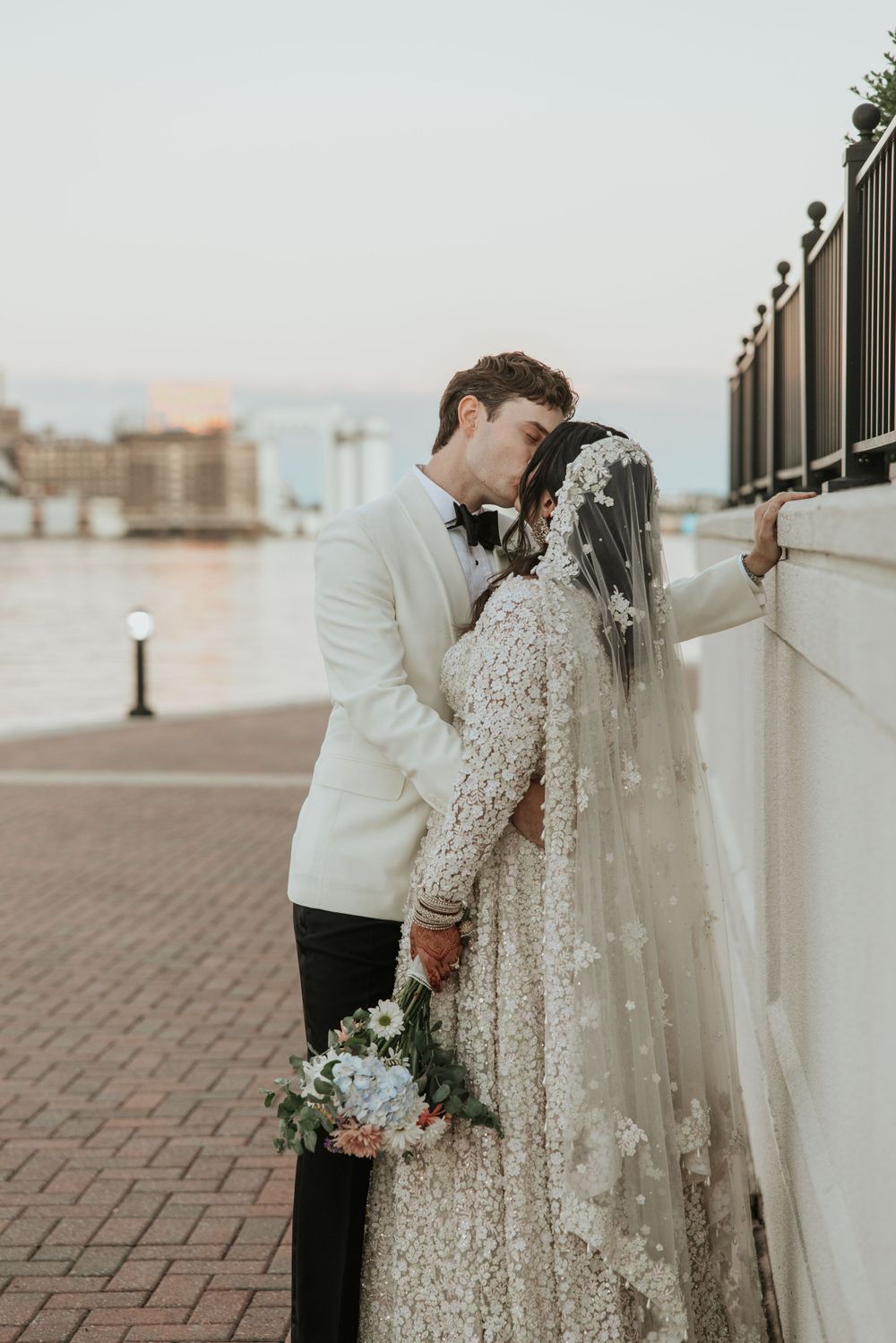 Romantic waterfront wedding portrait of couple sharing an intimate moment against a railing.