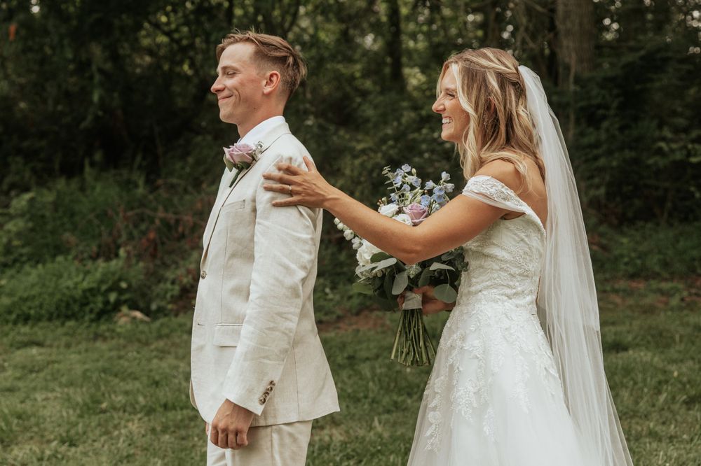 First look wedding moment captured in a garden setting with bride tapping groom's shoulder.