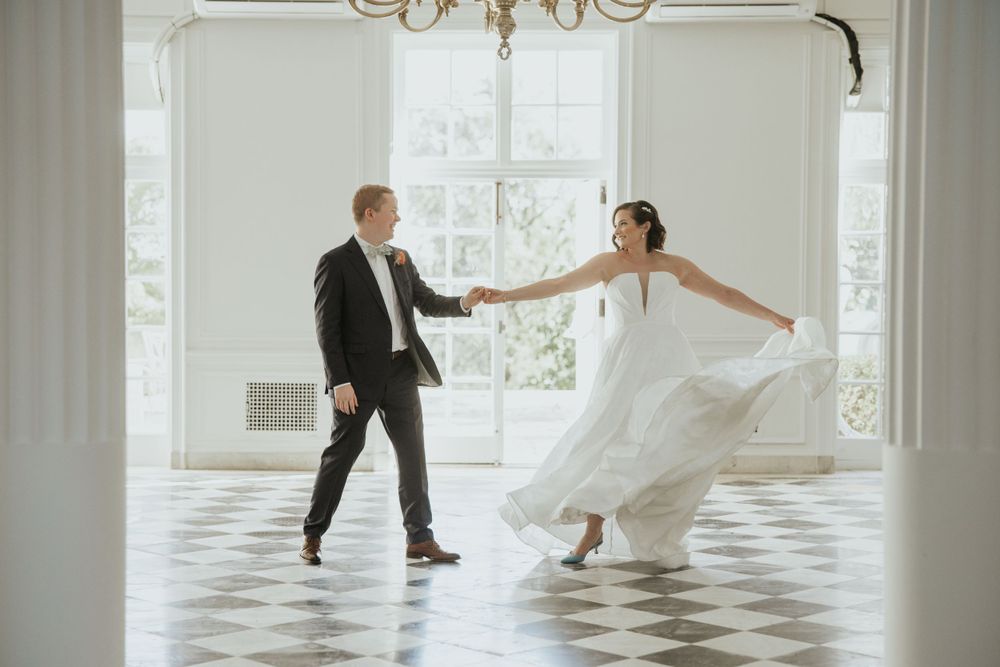 A couple dances playfully in a bright room with checkered floors and elegant decor.