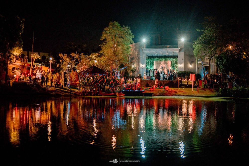 An outdoor evening wedding reception venue with colorful lights reflecting on a serene pond.