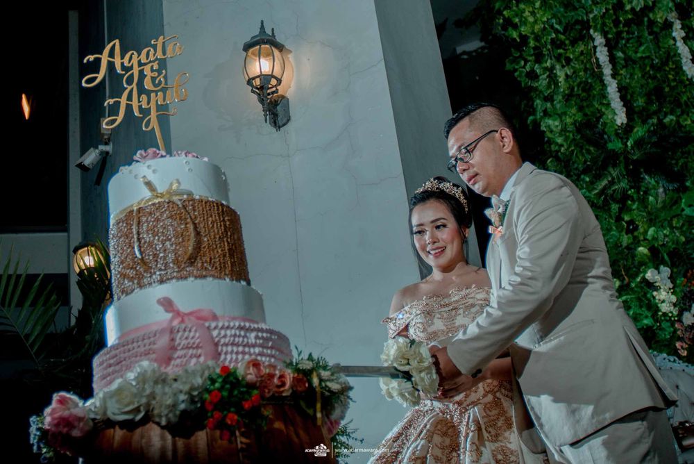 A couple cutting their elegant multi-tiered wedding cake beneath a decorative wall lamp.