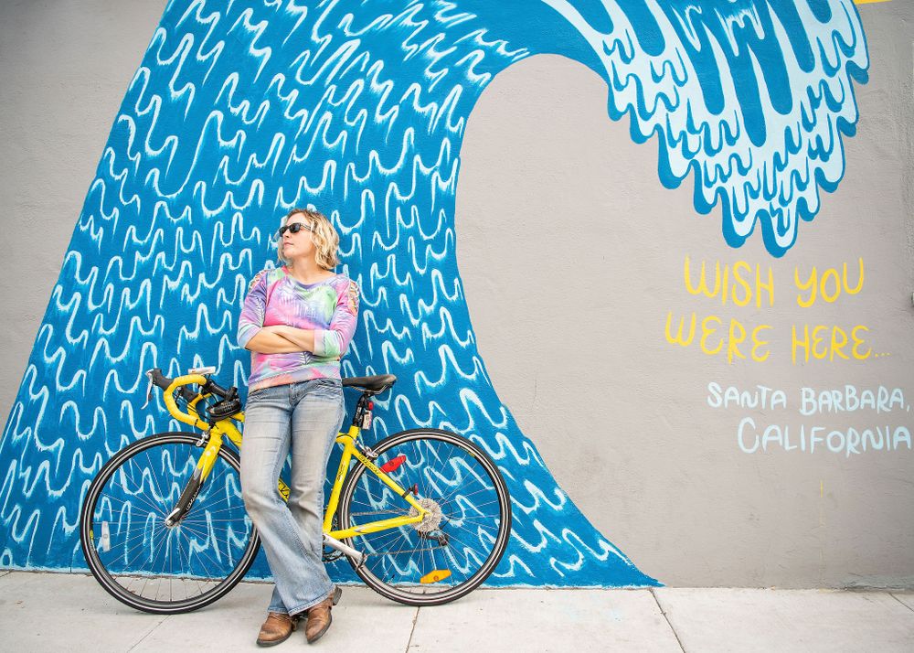 woman with a yellow bike parked in front of a wave mural outside in santa barbara ca