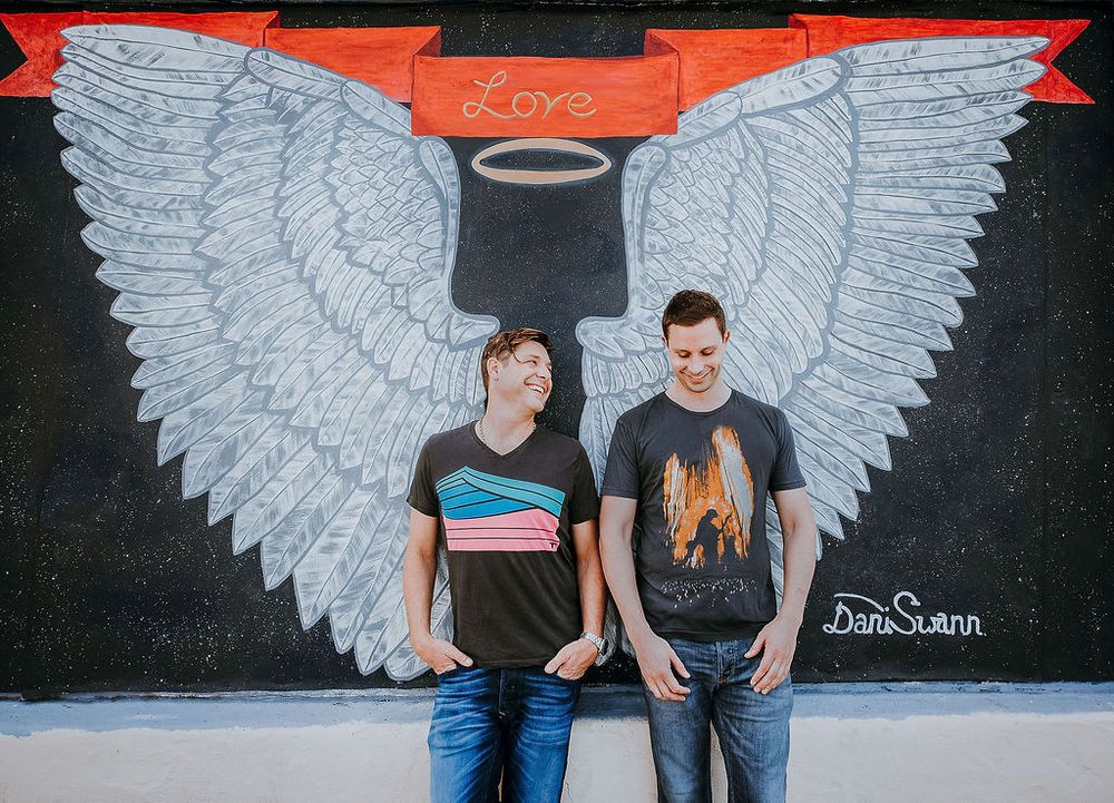 gay couple laughing candidly in front of angel wing mural santa barbara