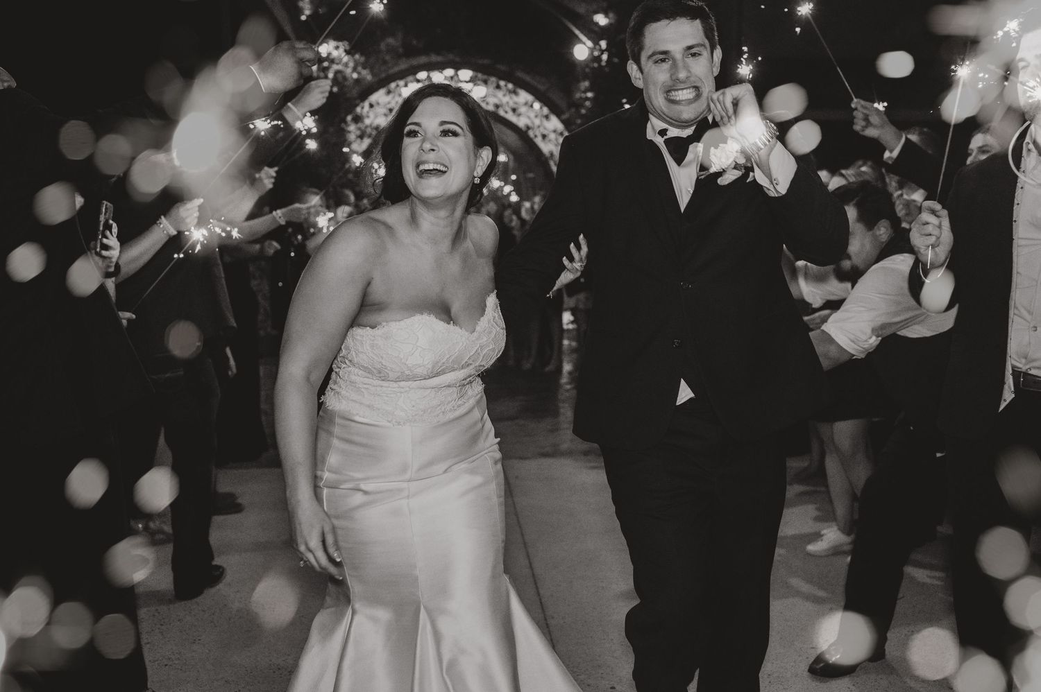 Couple making joyful exit through sparkling bokeh lights during wedding reception.