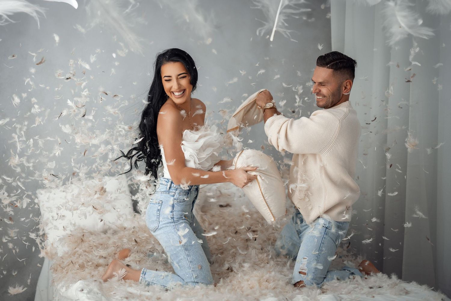 Playful couple having fun with feathers in a bright indoor setting.