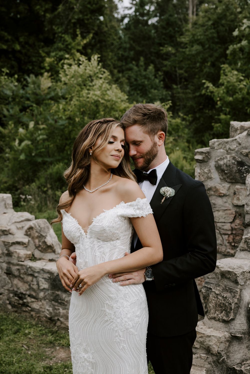 Intimate wedding portrait captured against stone walls and lush greenery.