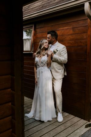 A couple in wedding attire embraces on a wooden deck.