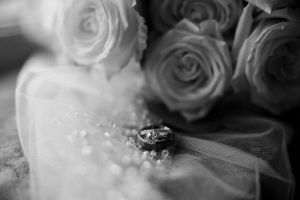 Wedding rings rest on delicate tulle veil with roses in soft focus background.