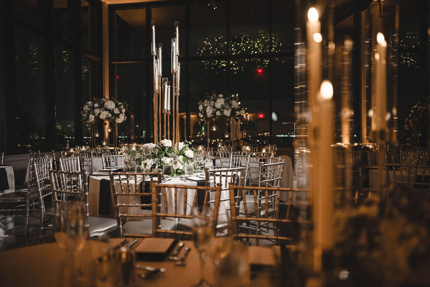 Romantic wedding reception venue with candlelit tables, floral centerpieces and silver chiavari chairs.