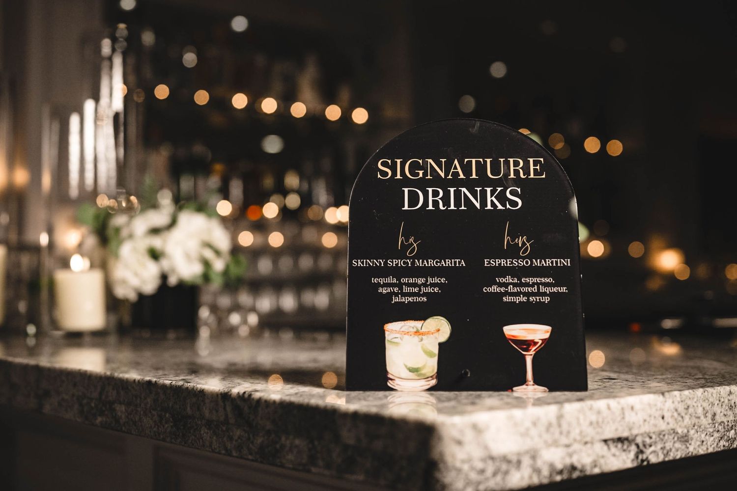 Signature drinks menu display on dark marble bar counter with cocktails in elegant glassware.