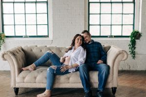 Couple relaxing together on a beige tufted couch in an industrial loft space with large windows.
