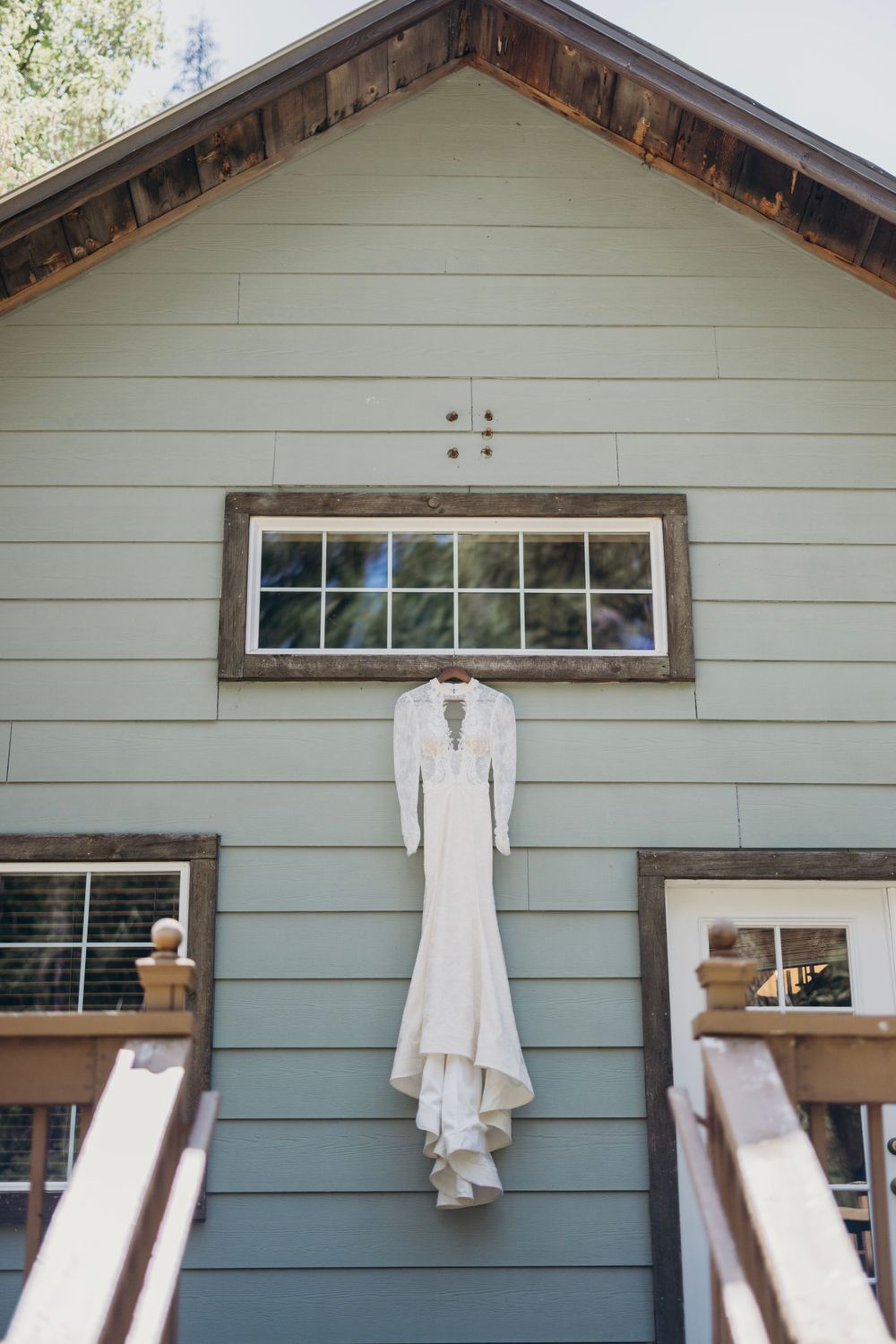 White wedding dress hanging on exterior wall of light blue house with rustic wooden trim.