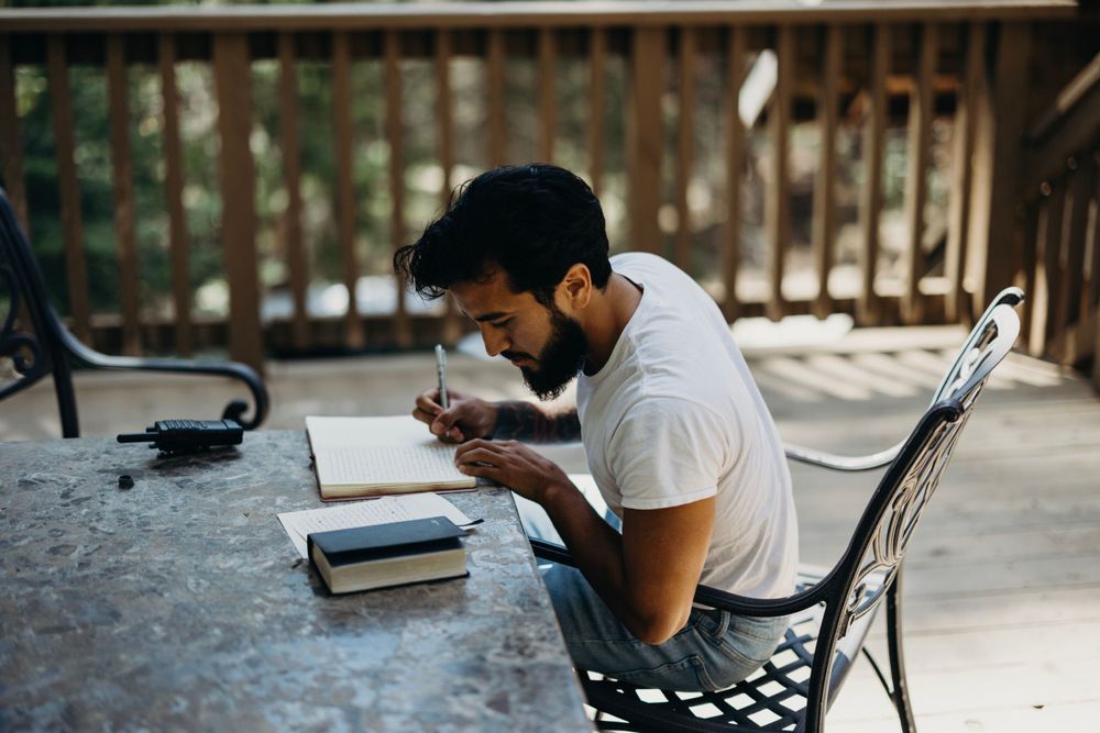 People writing in guest book at rustic wooden table during wedding reception.