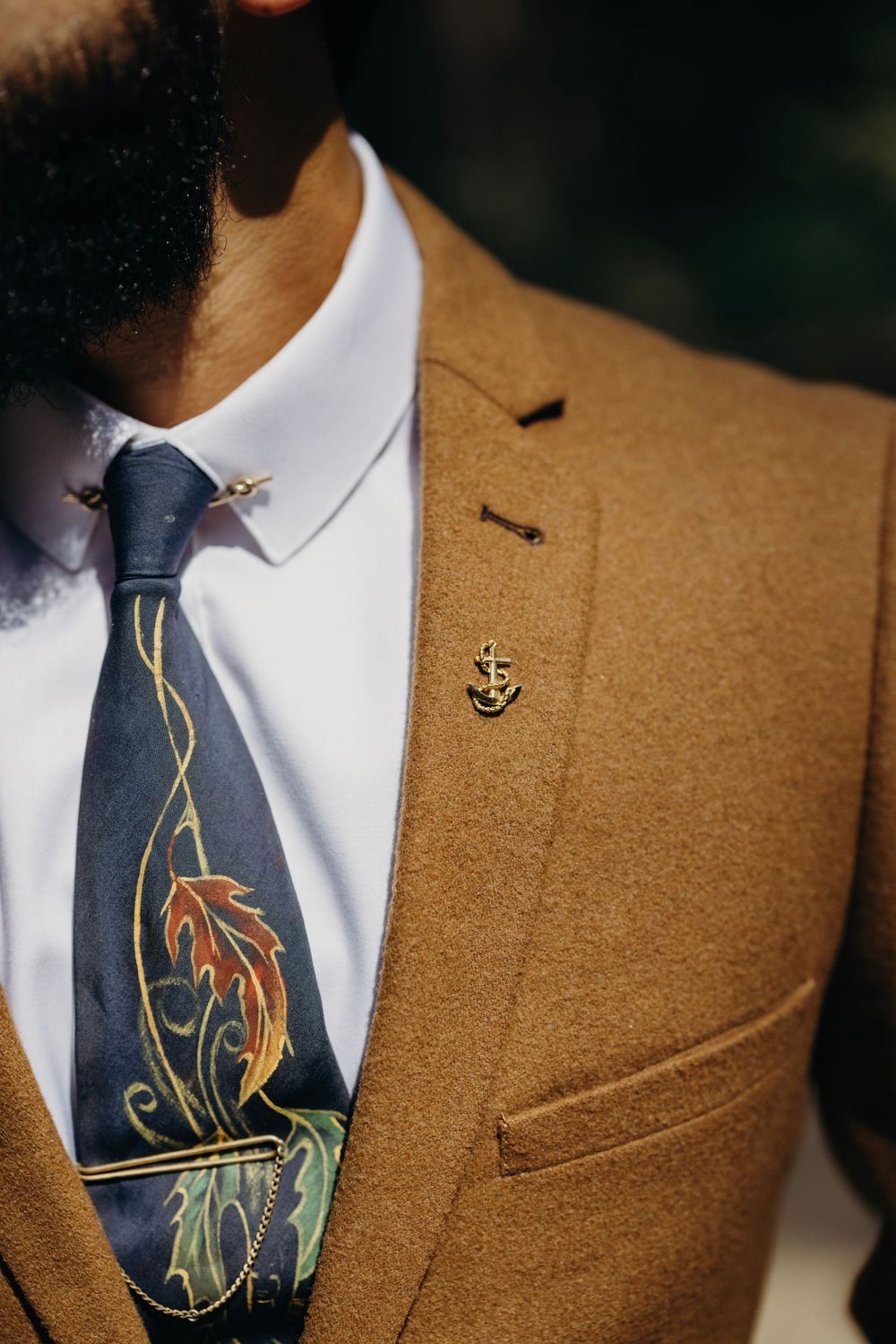 Close-up detail of navy tie with artistic fish design against brown suit jacket.