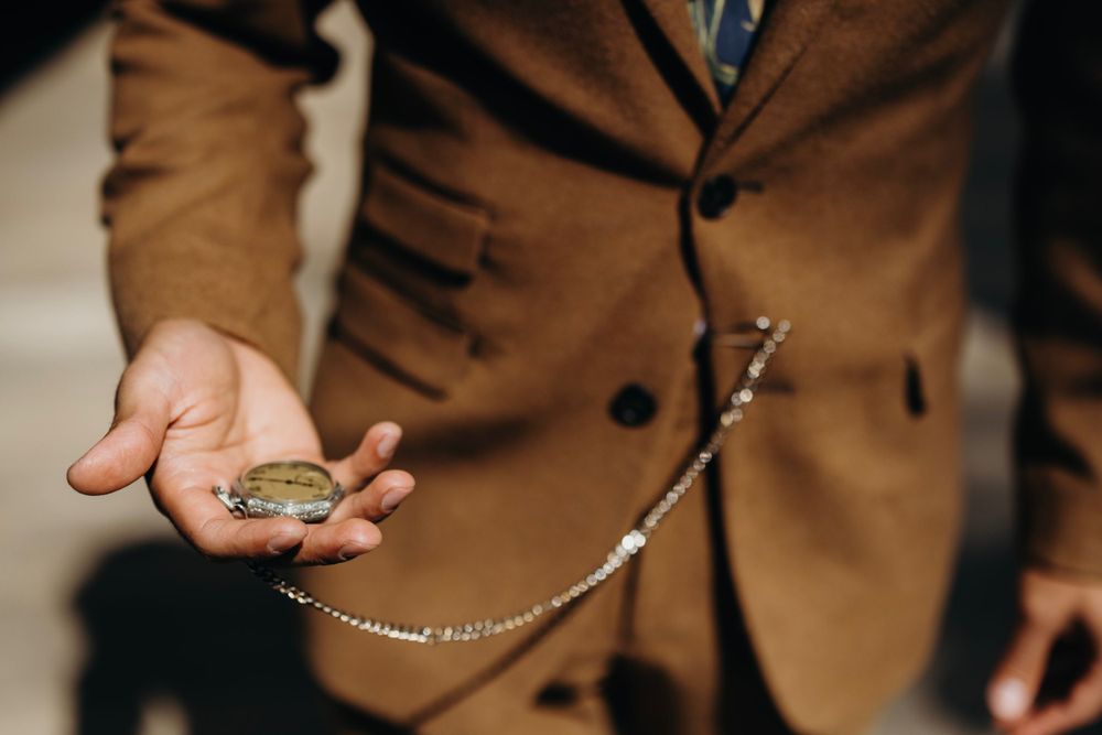 Hands holding delicate wedding jewelry and accessories against brown fabric.
