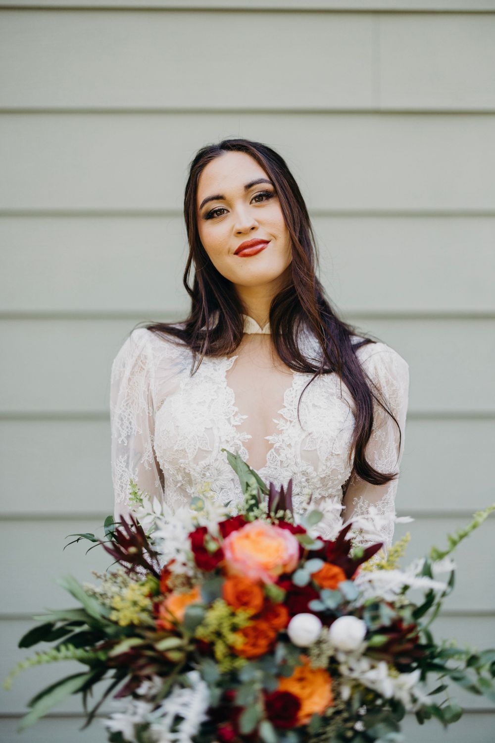 Bridal portrait with vibrant autumn-colored bouquet against white siding.