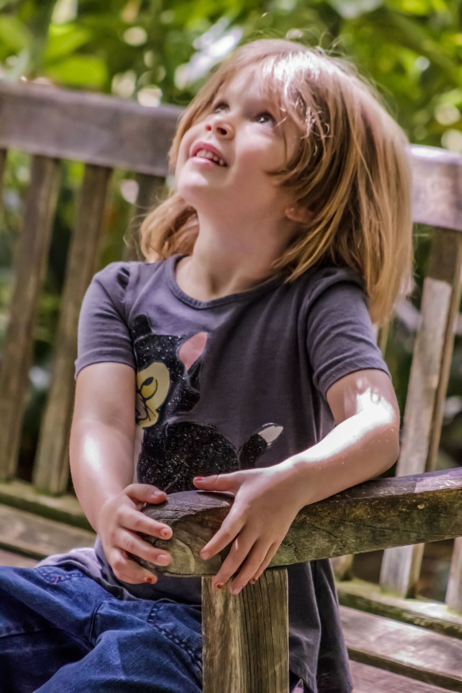 Young child laughing joyfully while sitting on a wooden bench outdoors.