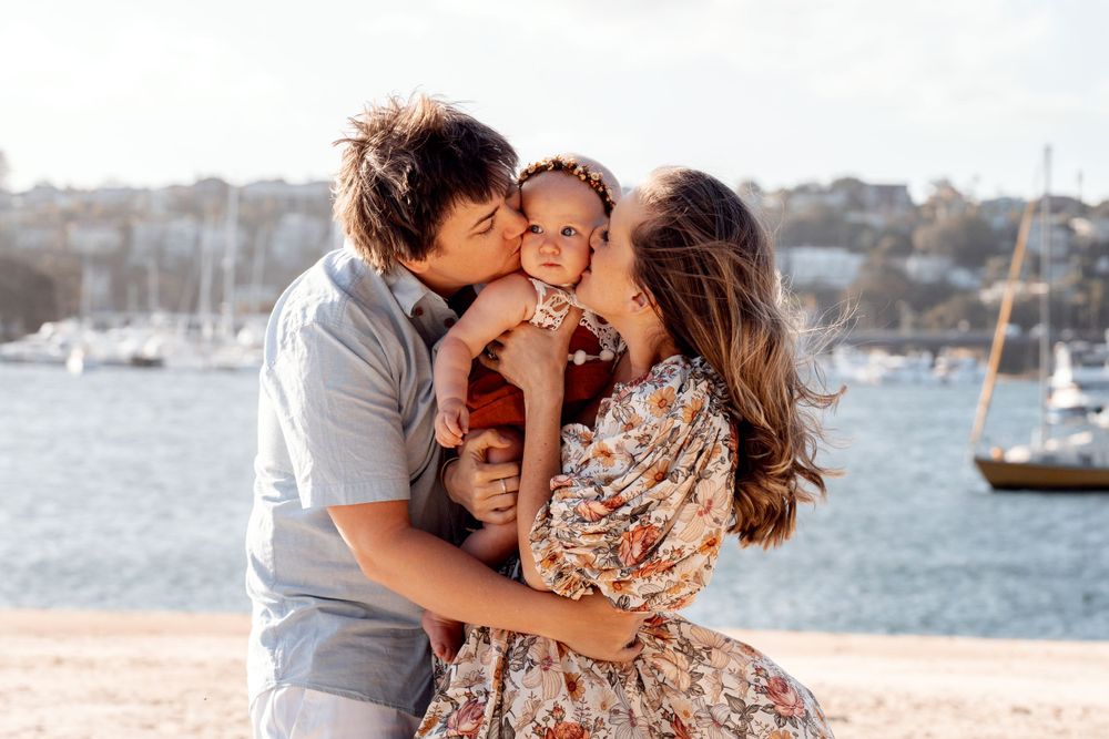 Mom and dad kissing baby during a family photoshoot