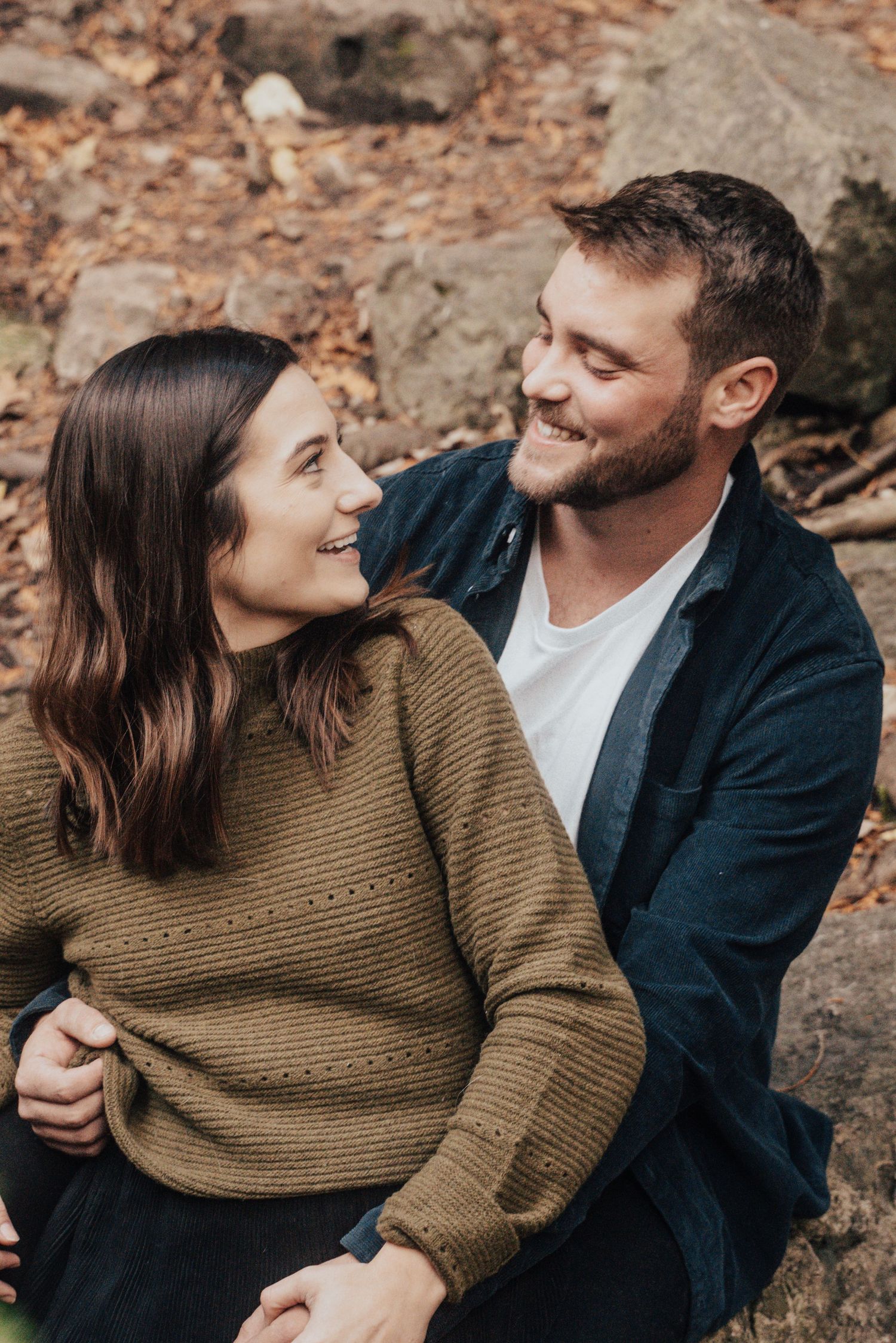 Image of woman and man smiling at eachother in forest.