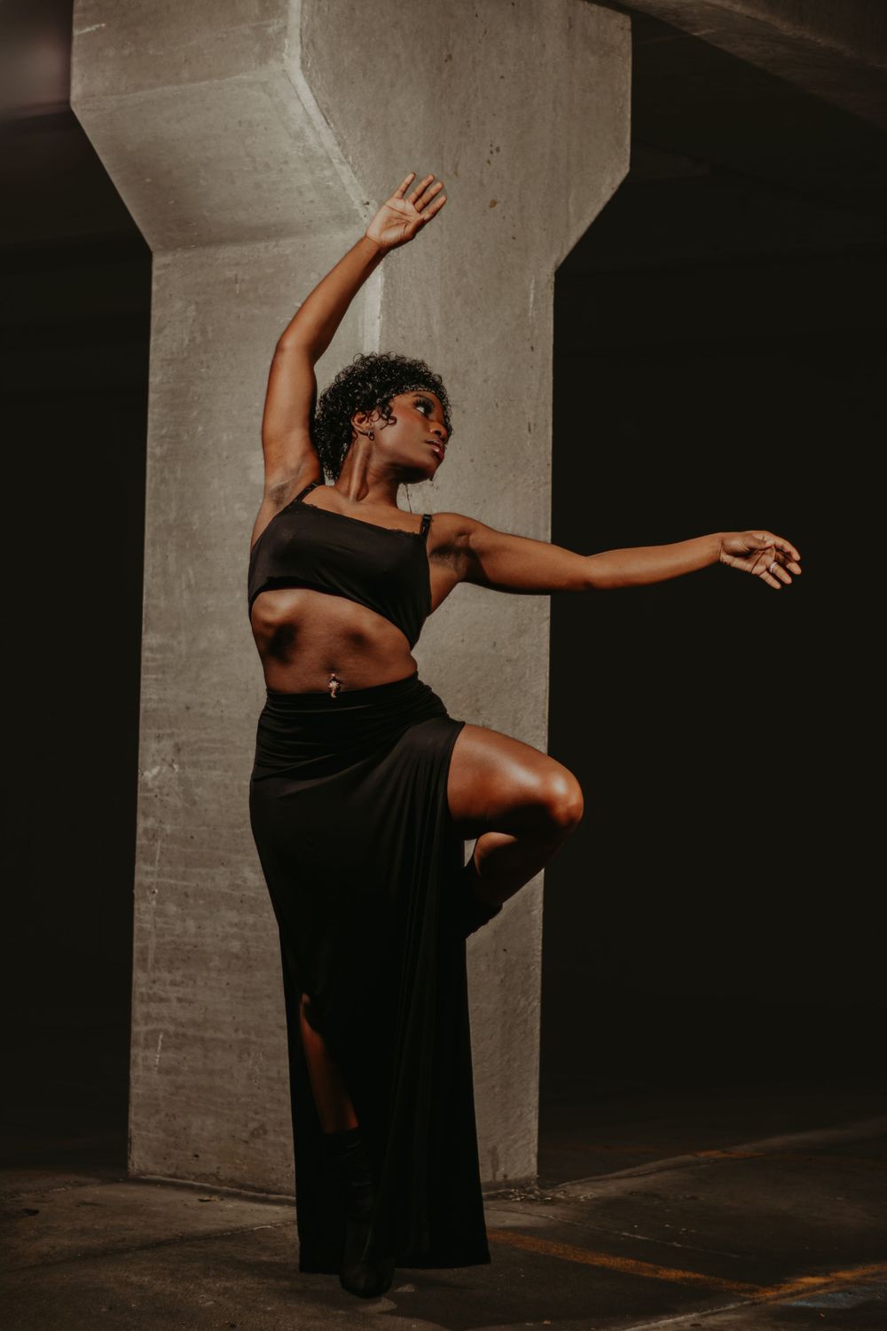Dynamic dance pose captured against concrete pillar shows graceful movement in black outfit.