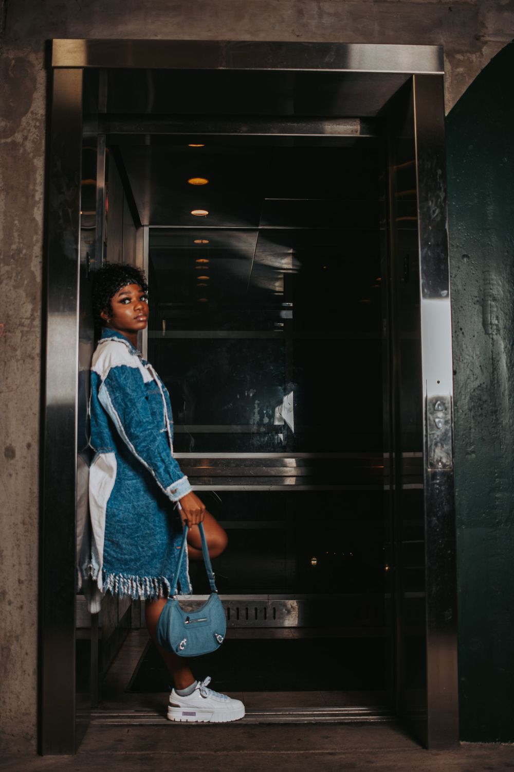Child in denim overalls standing by concrete pillars in a dark interior space.