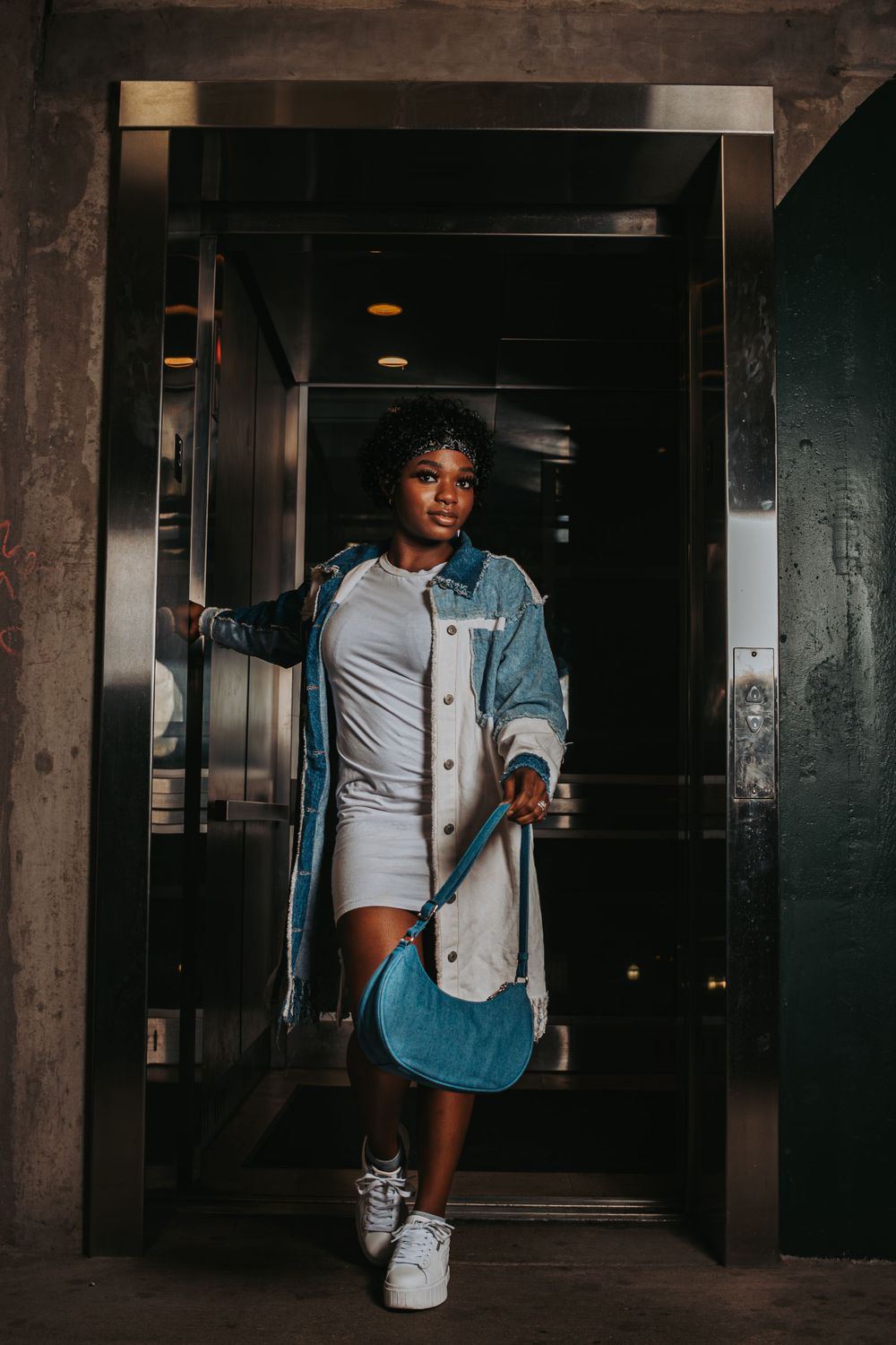Model in casual denim outfit poses confidently in industrial elevator doorway.