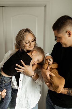 A family shares an intimate moment at home while holding a small child and playing with a stuffed animal.