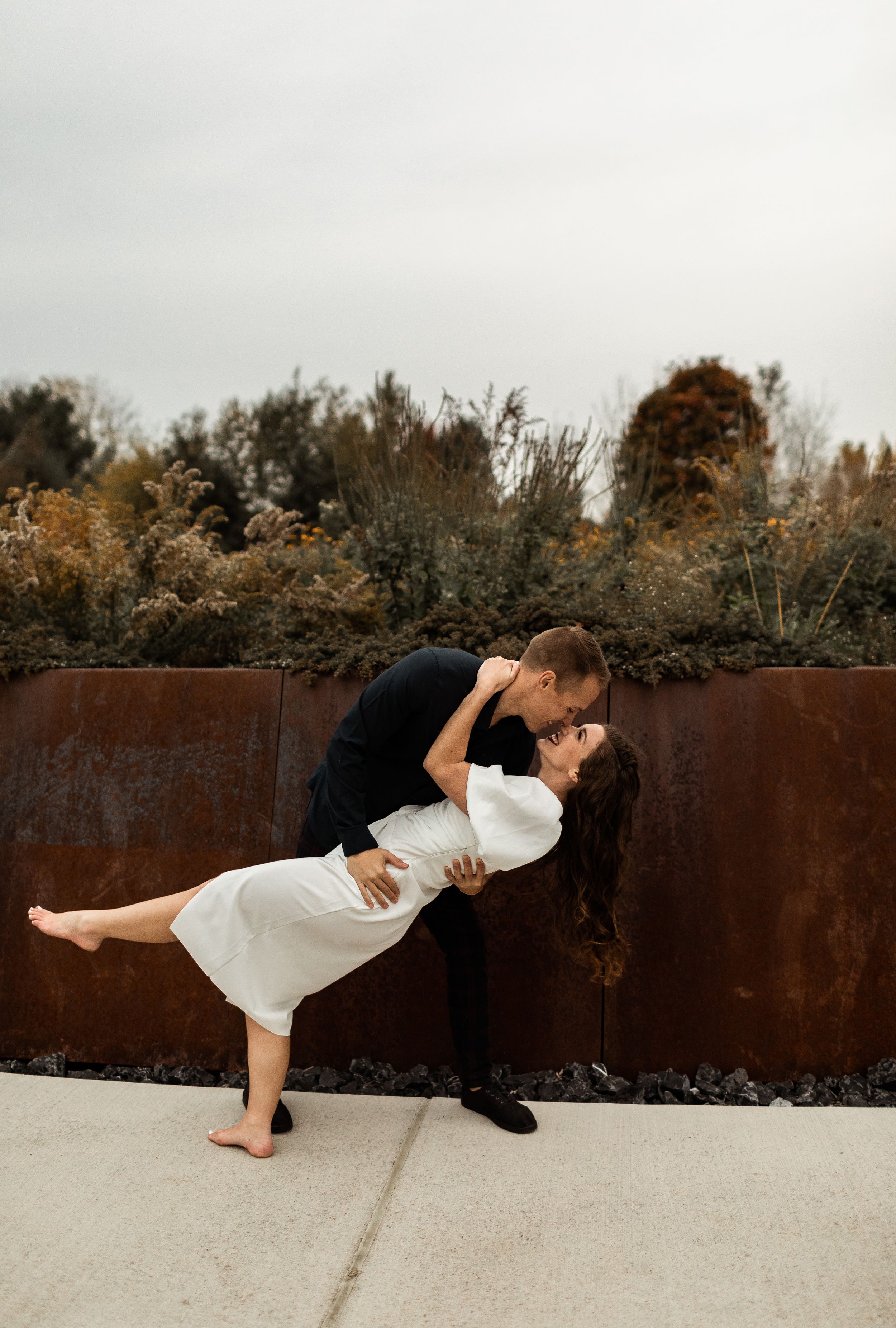 Romantic dip pose against rustic metal wall during sunset photoshoot.