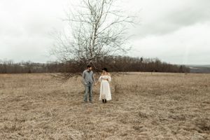 A couple standing together in a barren winter field under cloudy skies.