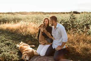 A couple sits outdoors at sunset with their dog enjoying a picturesque moment in a golden field.