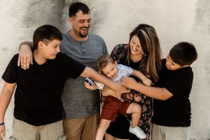 Candid family moment captured against neutral wall showing playful interaction.