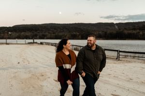Couple walking and laughing together along waterfront path with lake view.