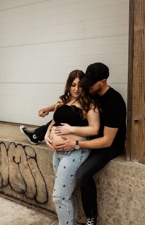 A couple sitting together against a white wall while dressed casually in black and denim.