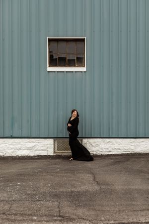 Artistic portrait of woman in black dress against industrial metal wall with small window.