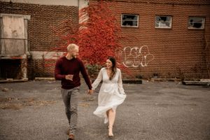Couple running playfully together against brick wall with vibrant red autumn vines.