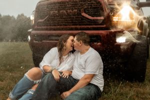 A couple shares an intimate moment in front of a vintage truck during a rainy sunset.