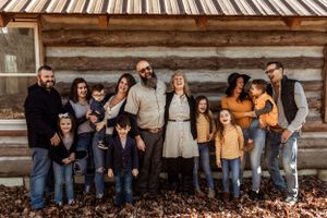 A large group poses together against a rustic log cabin wall during an autumn photoshoot.