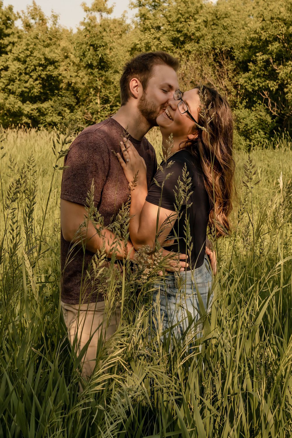 A romantic couple embracing and kissing in a golden field of tall grass at sunset.