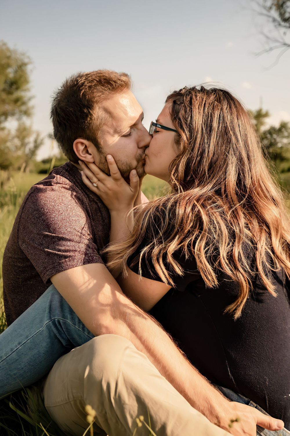 A tender moment between a couple sharing a passionate kiss in a sunlit field.