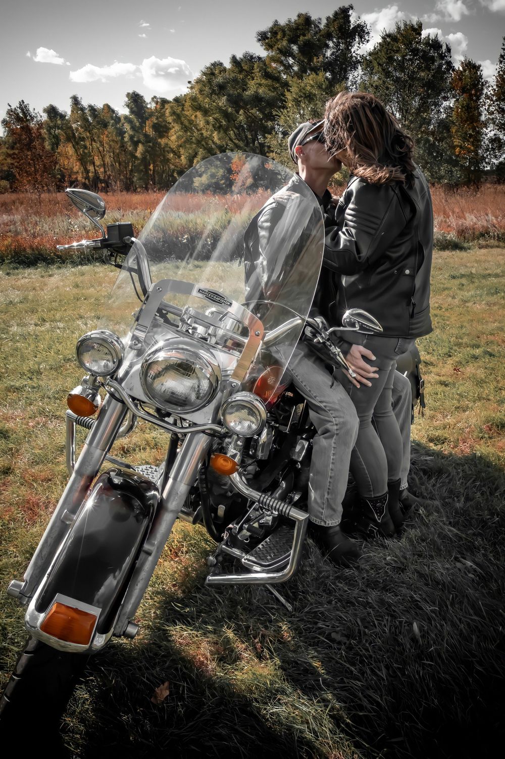 A couple sharing an intimate moment while sitting on a motorcycle in a rustic field.