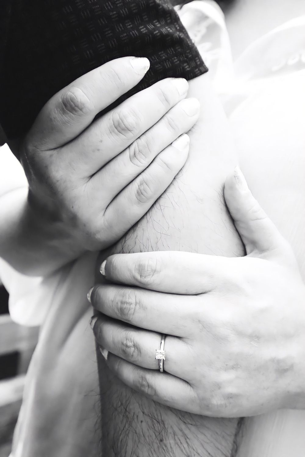 Close-up black and white photo of hands with wedding ring in an intimate embrace.