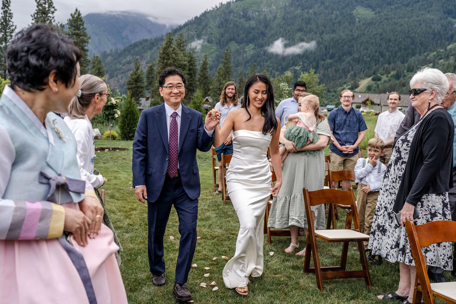 Outdoor wedding ceremony in front of misty mountain backdrop with wooden chairs on green grass.