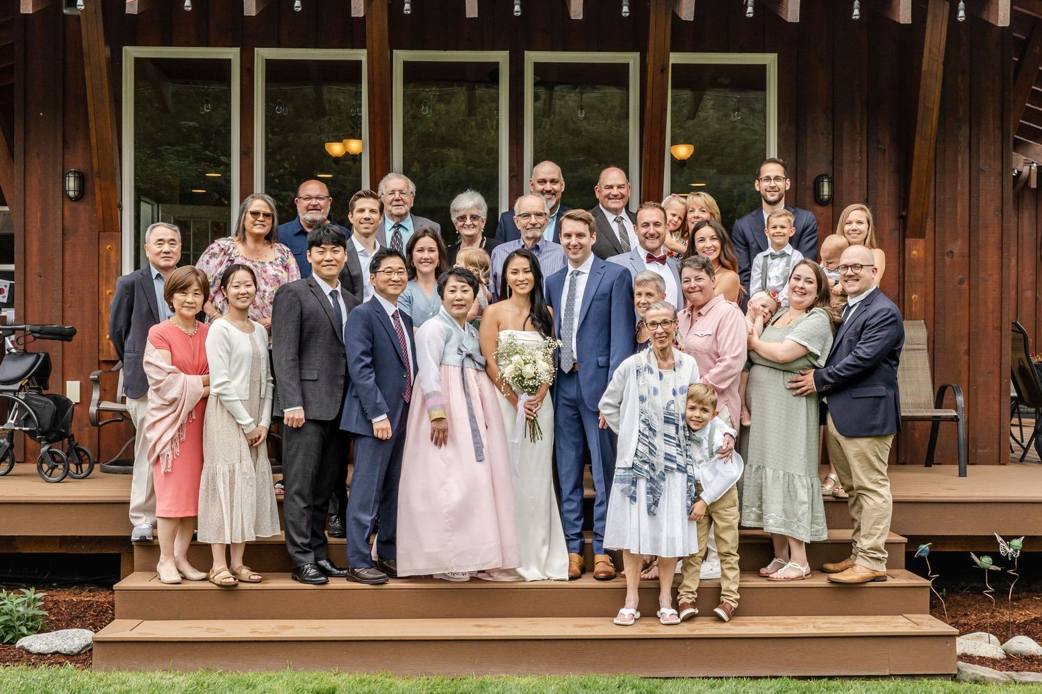Wedding party group photo on wooden deck steps with rustic building background.