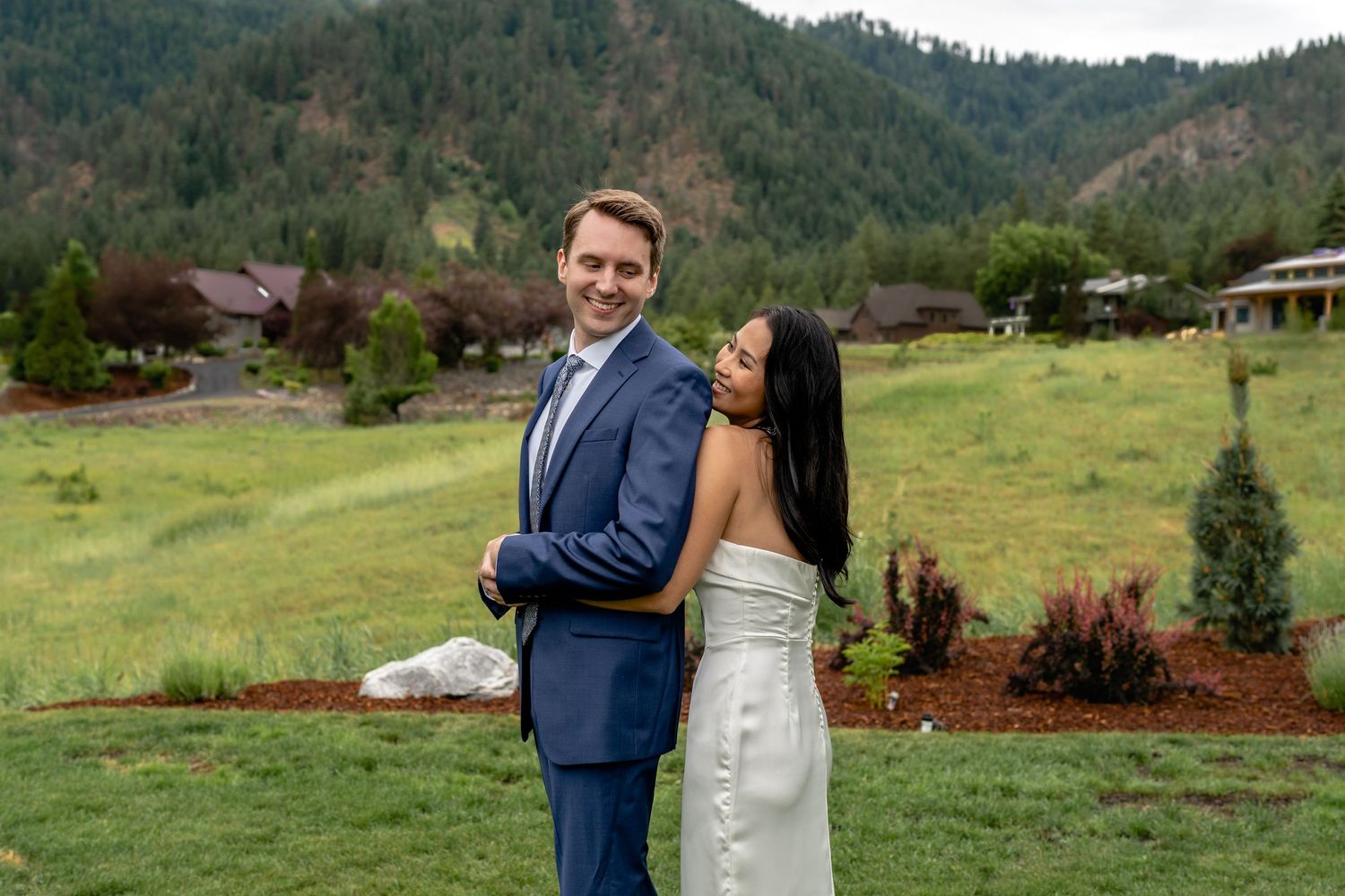 Couple embracing in elegant attire against mountainous landscape and green meadow.